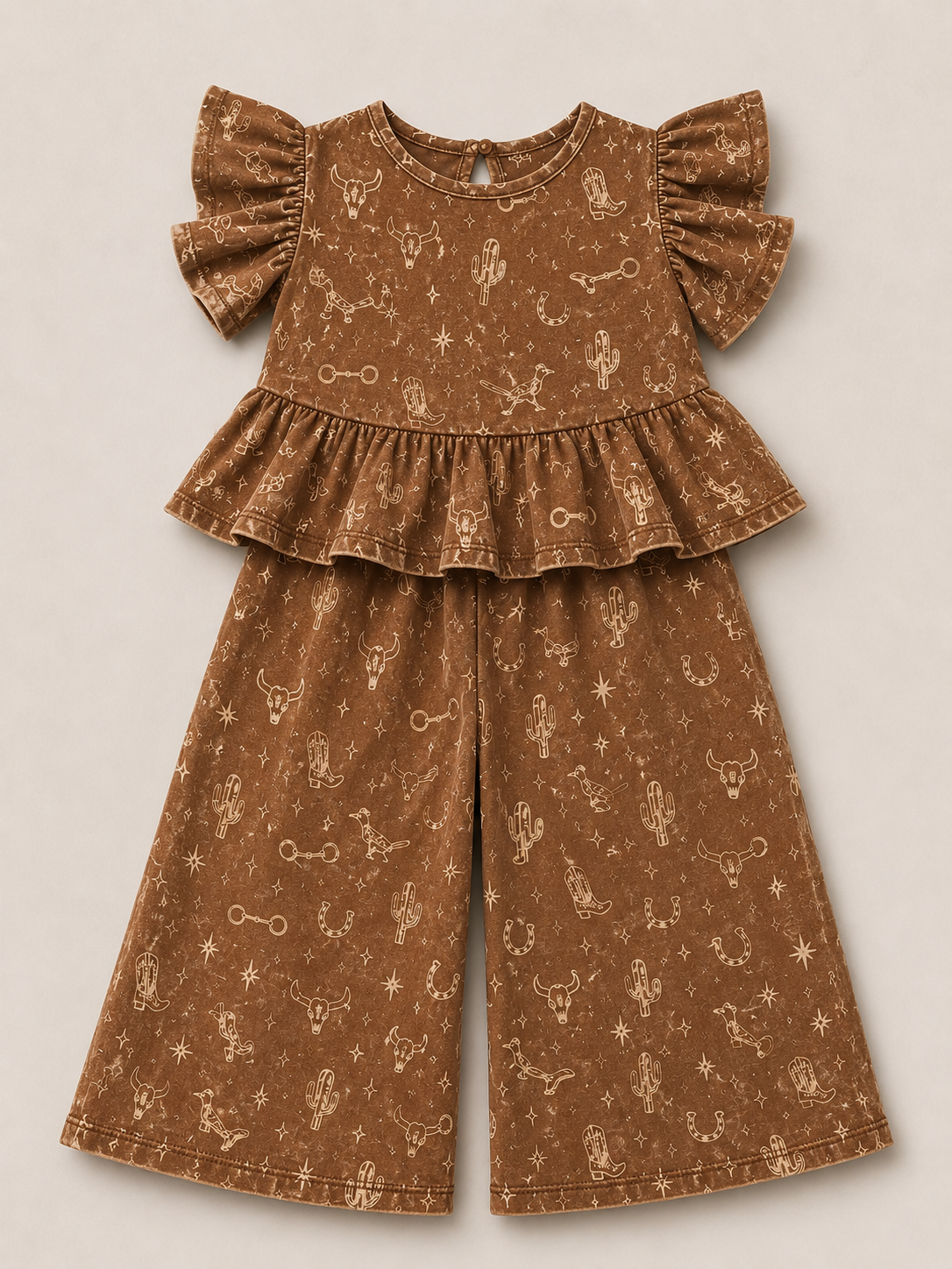 A two-piece outfit set in a brown fabric with a light beige western-themed print of cacti, stars, and bones. The set includes a short-sleeve top with ruffled shoulders and a matching pair of wide-leg pants, laid flat on a neutral beige background.