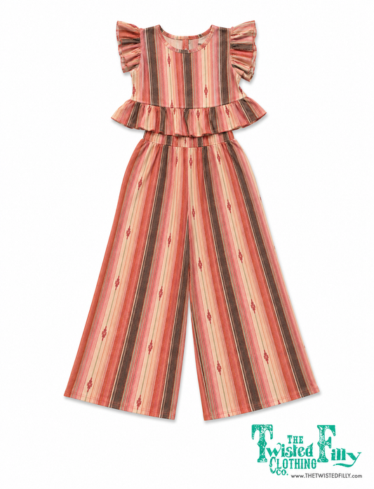 A children's sleeveless jumpsuit with ruffled shoulders and wide legs, featuring vertical stripes in terracotta, pink, beige, and brown with small diamond motifs, shown on a white background  