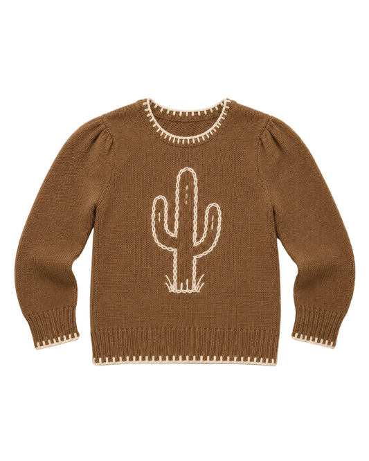 A brown knit sweater with a white cactus design on the front, featuring decorative white stitched trim around the neckline, cuffs, and hem, laid flat on a light beige textured background.